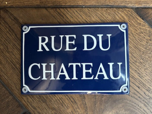 Blue sign with white text 'RUE DU CHATEAU' on a wooden background